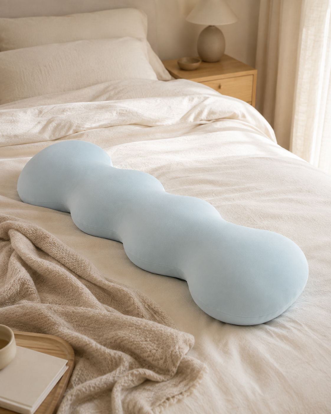 Blue Snuggle Buddy body alignment pillow lying on a neutral bed