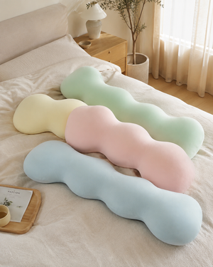 Snuggle Buddy body alignment pillows in mint green, pink, blue and yellow on a bed